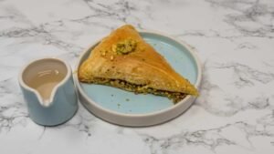 Pistachio Baklava – Traditional Middle Eastern Dessert Traditional Middle Eastern baklava filled with chopped pistachios, served on a blue plate with syrup.