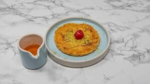 Traditional Middle Eastern kunafa dessert topped with crushed pistachios and a red cherry, served with sugar syrup.
