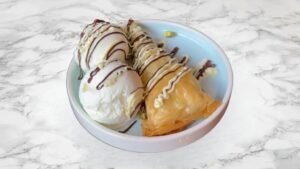 Traditional baklava served with vanilla ice cream, pistachios and chocolate and white chocolate drizzle