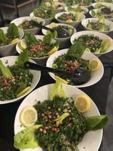 Fresh tabouleh salad served in white bowls with romaine lettuce, lemon wedges, and pomegranate seeds, arranged for catering.