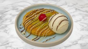 Traditional kunafa topped with pistachio, chocolate and white chocolate drizzle, served with vanilla ice cream and a cherry