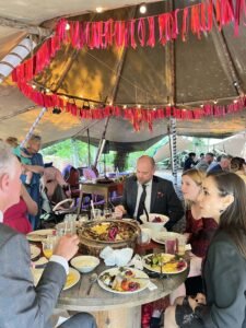 Guests enjoying a catered dinner together under a decorated outdoor tent with colorful ribbon garlands and string lights.